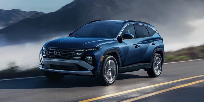 Blue Hyundai Tucson SUV driving on a paved highway with mountains in the background.