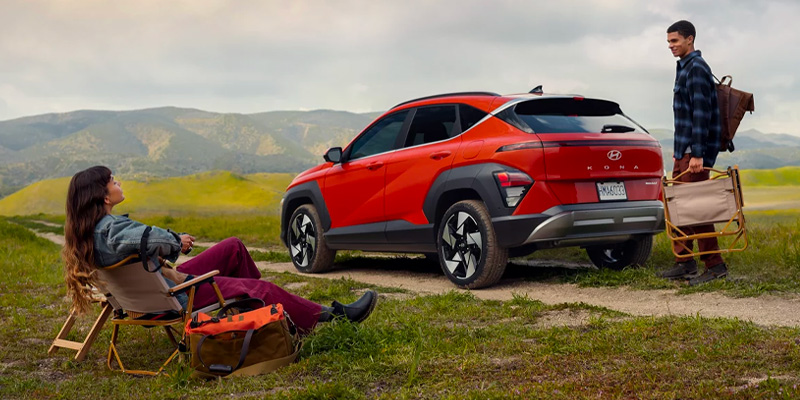 A red 2026 Hyundai Kona parked next to two individuals sitting on a bench in Wichita Falls, TX.